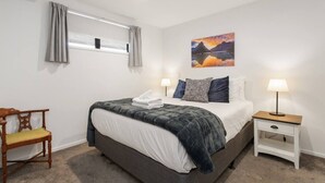 A bedroom with a bed, bedside table, chair, and a painting on the wall. - Modern Townhouse  Walk to Hagley Park & Hospital (Christchurch)