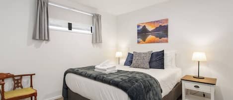 Un dormitorio con cama, mesita de noche, silla y un cuadro en la pared.