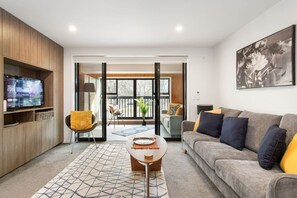Ein modernes Wohnzimmer mit einer Couch, einem Couchtisch, einem Fernseher und einer Glastür zum Außenbereich.