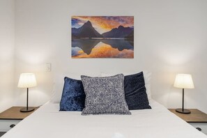 Ein Bett mit weißer Bettwäsche, zwei Nachttische mit Lampen und ein Gemälde von Berg und See an der Wand.