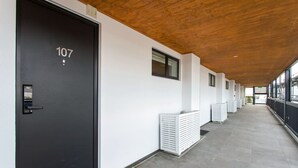 Un pasillo con una puerta negra marcada '107', paredes blancas y techo de madera.