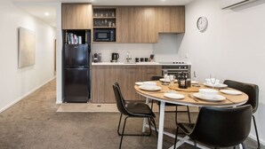 Una cocina compacta con electrodomésticos modernos, una mesa de comedor lista para cuatro personas y un reloj en la pared.