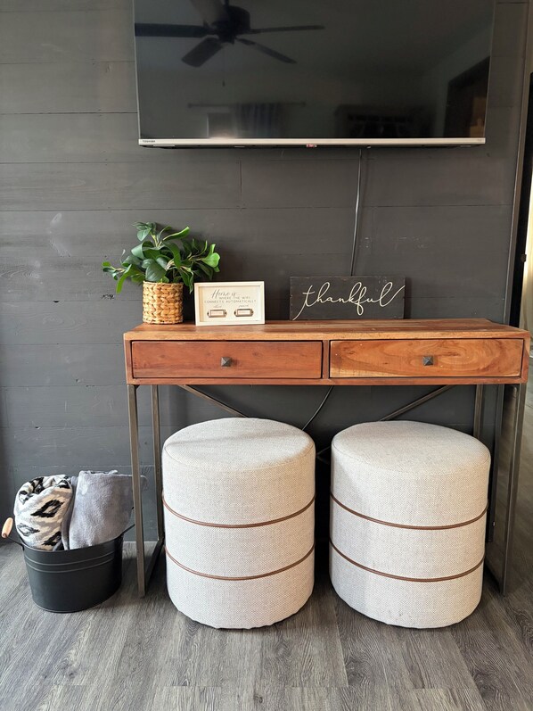 A wooden desk with two round ottomans, a woven plant pot, a framed sign, and a wall-mounted TV. - Delightful 3-bedroom house in Rapid City perfect for your getaway (Rapid City)