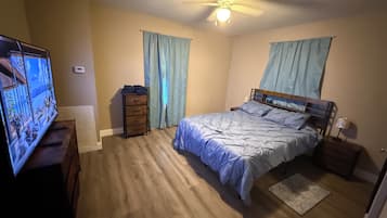 Un dormitorio con cama, televisión, cómoda y ventilador de techo.