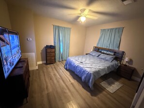 A bedroom with a bed, a television, a dresser, and a ceiling fan.