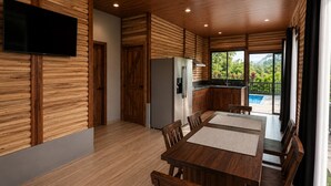 A modern kitchen with wooden paneling, a dining area with a wooden table and chairs, and a view of a swimming pool.