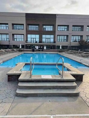 A rectangular swimming pool with steps leading up to it, surrounded by lounge chairs and umbrellas.