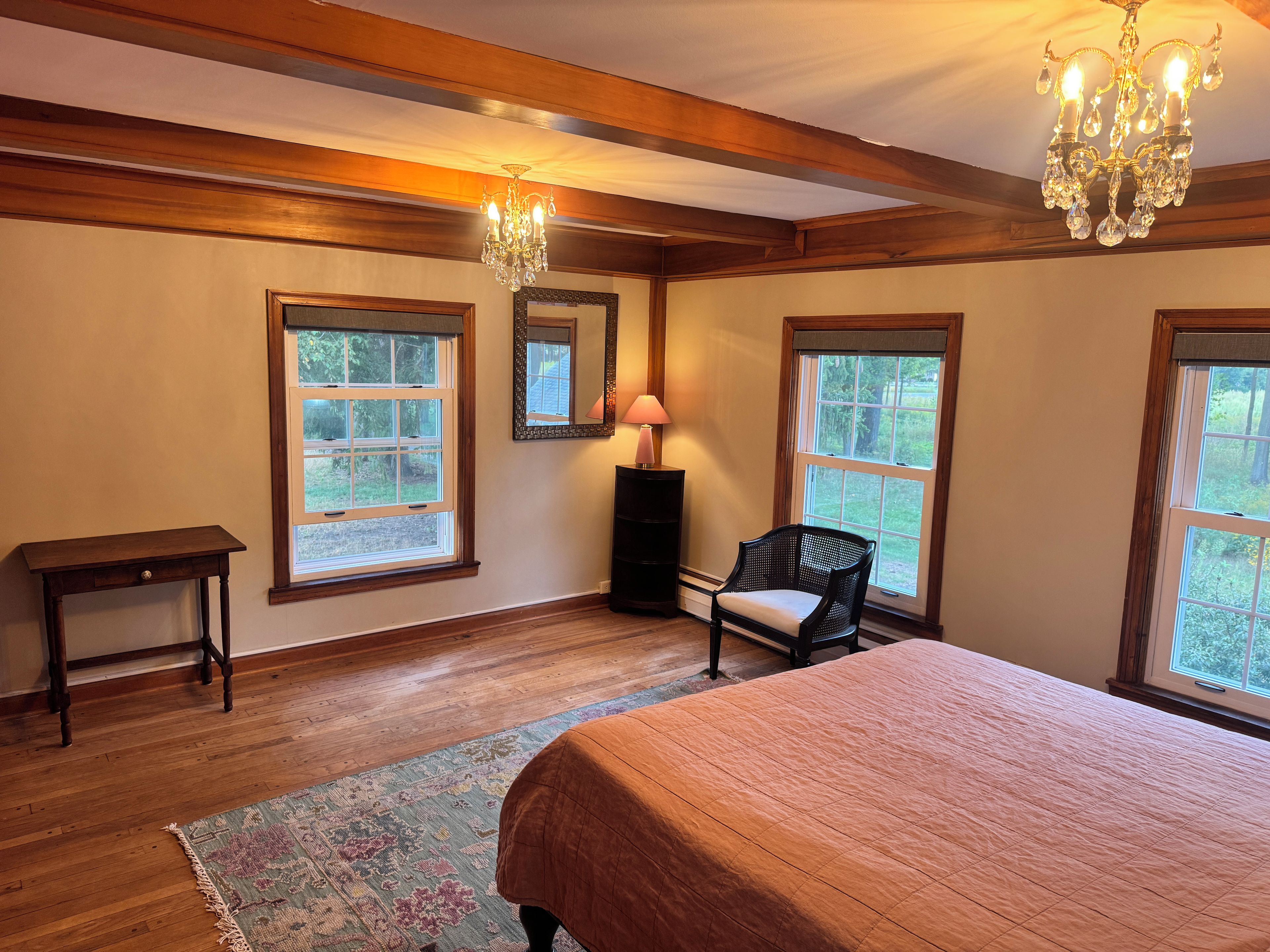 Une chambre avec un grand lit, un plancher en bois, un lustre et deux fenêtres.