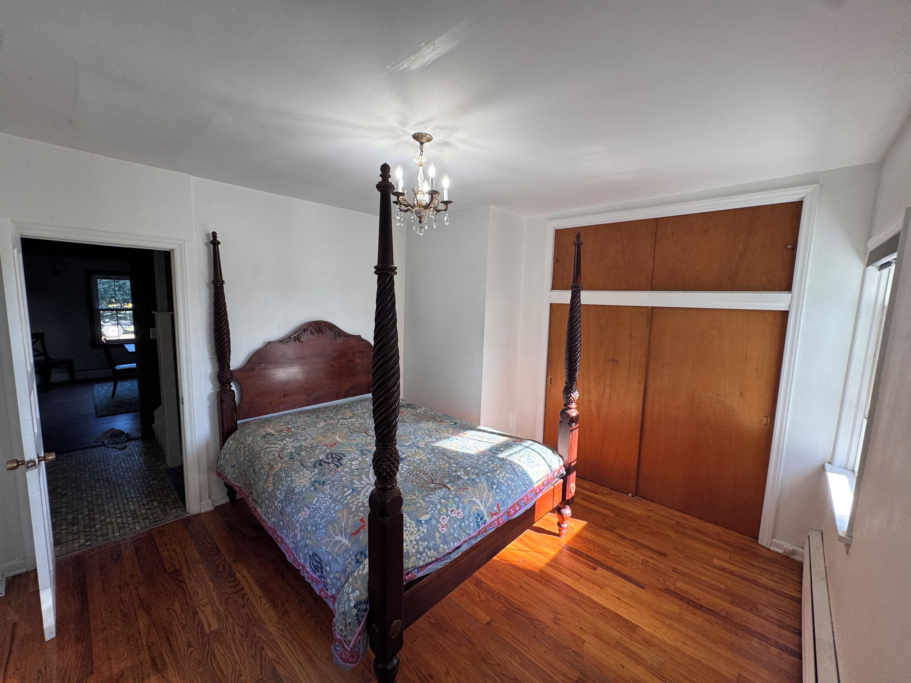 A four-poster bed with a chandelier, wooden flooring, and a closet with a wooden door.