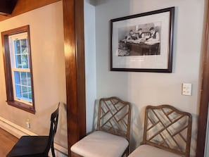 Una habitación con una fotografía histórica enmarco, dos sillas de madera, un ventanal y una puerta.