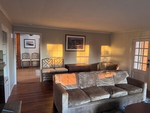 A living room with a sofa, two armchairs, a coffee table, and a fireplace. There are framed pictures on the wall and a door with a window.