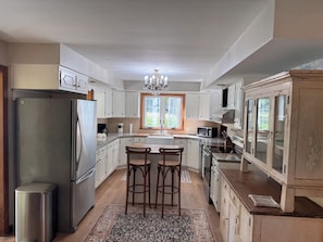 A kitchen with white cabinets, a stainless steel refrigerator, a chandelier, and a window with a view.