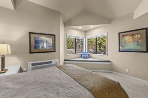A bedroom with a large bed, a window seat with a view of trees, and two framed pictures on the walls. - River Ridge 420AB - Spacious River View Condo w/Seasonal Pool & Hot Tub Near the Old Mill (Bend)