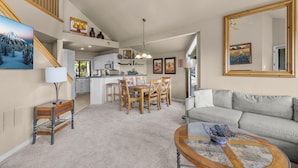 A spacious living area with a sofa, a coffee table, and a dining table with chairs. There is a kitchen area with cabinets and a dining table.