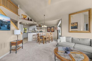 A spacious living area with a sofa, a coffee table, and a dining table with chairs. There is a kitchen area with cabinets and a dining table.