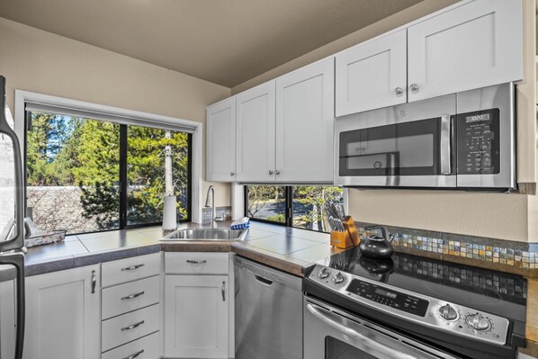A modern kitchen with white cabinets, a stainless steel range, a microwave, and a dishwasher. - River Ridge 420A - Prime Westside River Views | Pool & Hot Tub (Bend)