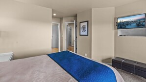 A bedroom with a bed, a television, and a door leading to another room. - River Ridge 420A - Prime Westside River Views | Pool & Hot Tub (Bend)