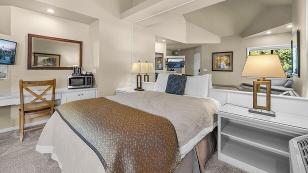 A hotel room with a bed, bedside tables, a chair, a desk, a microwave, a TV, and a large mirror. - River Ridge 420B -Westside Studio, Pool & Hot Tub (Bend)