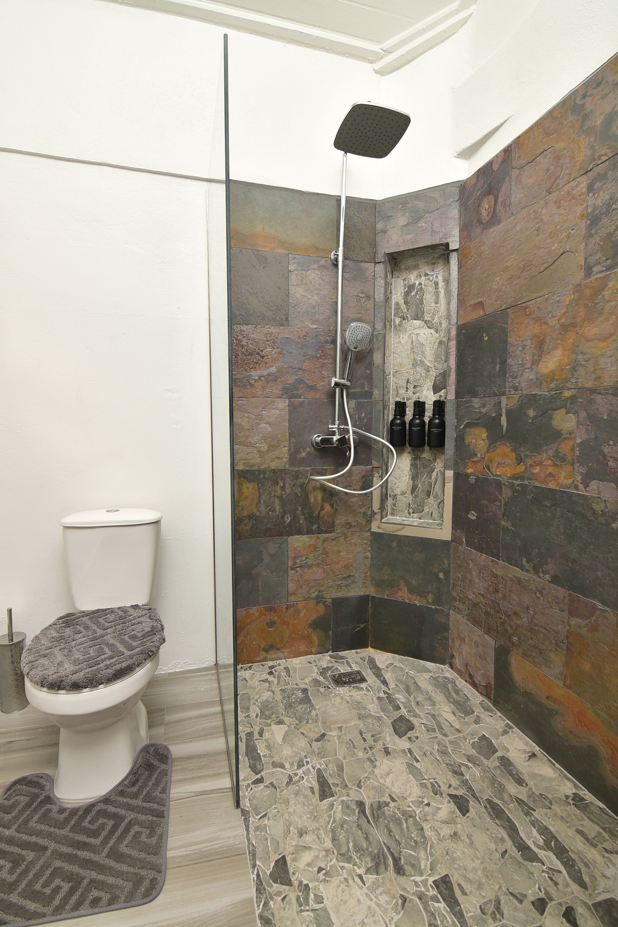 Een badkamer met douche, toilet en een klein plankje met flessen.
