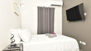 Une chambre d’hôtel équipée d’un lit, d’un téléviseur fixé au mur, d’un climatiseur et d’une petite table avec une télécommande.