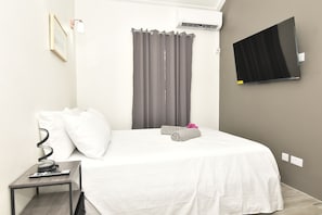 Ein Hotelzimmer mit einem Bett, einem an der Wand befestigten Fernseher, einer Klimaanlage und einem kleinen Tisch mit einer Fernbedienung.