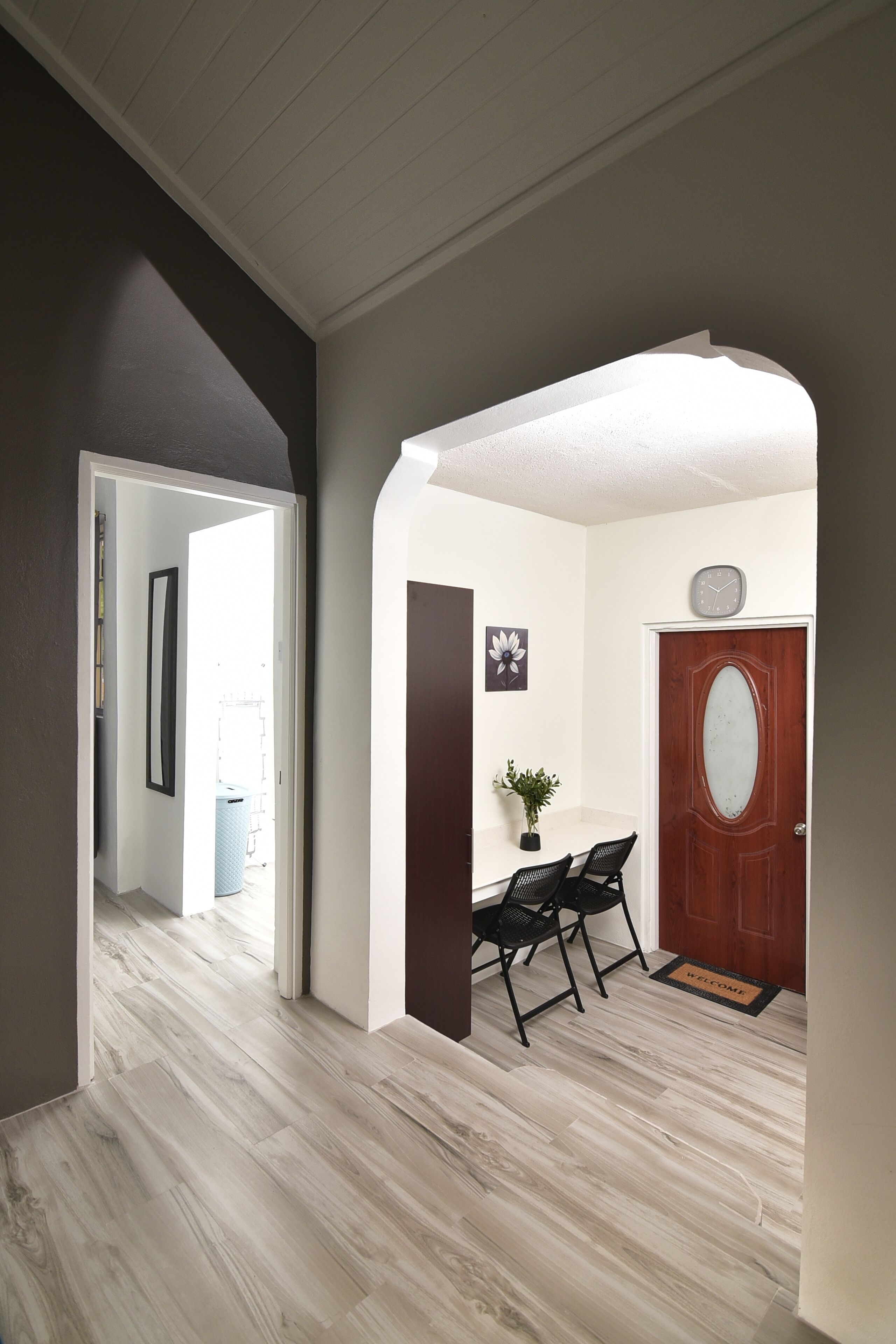 A hallway with a wooden floor, a white door with a glass panel, and a small table with two chairs.