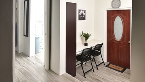 Un couloir doté d’un plancher en bois, d’une porte blanche avec un panneau de verre et d’une petite table accompagnée de deux chaises.