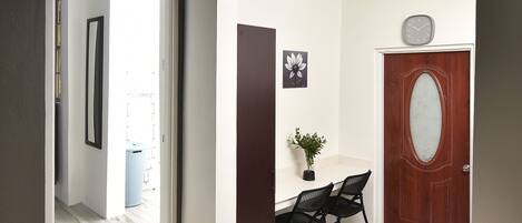 A hallway with a wooden floor, a white door with a glass panel, and a small table with two chairs.