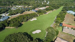 Oversigtsbillede af en golfbane med flere sandbunker, omgivet af beboelsesejendomme og frodig vegetation.