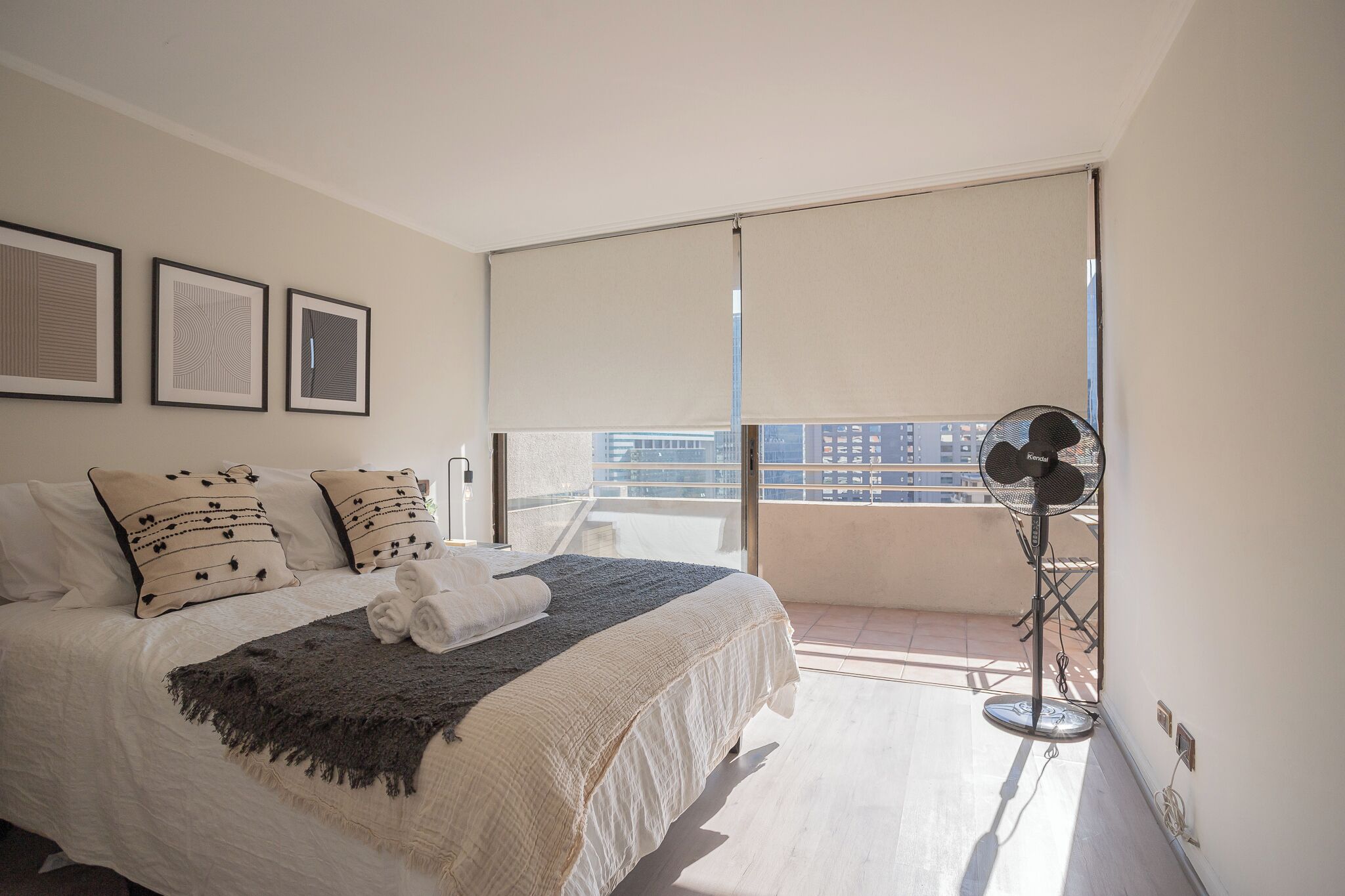 Un dormitorio con cama, lámpara de pie y ventana con vistas a edificios.