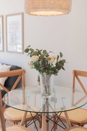 A round glass table with a clear vase containing white flowers and green leaves. - San Sebastian Apartments By Andes (Las Condes)
