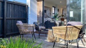 Eine Terrasse im Freien mit Korbmöbeln, einer Glastür zu einem Wohnbereich und einem Holzboden.