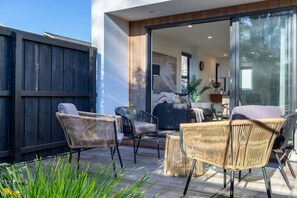 An outdoor patio with wicker furniture, a glass door leading to a living area, and a wooden deck. - Peaceful Merivale Hideaway - Parkside + Parking (Christchurch)