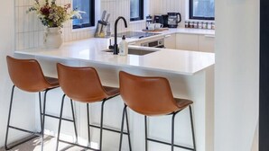 Eine moderne Küche mit Kochinsel, Barhocker und einer Kaffeemaschine.
