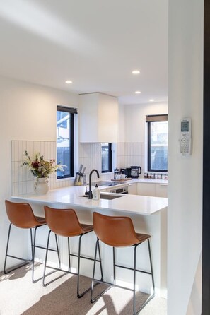 A modern kitchen with a central island, bar stools, and a coffee machine. - Peaceful Merivale Hideaway - Parkside + Parking (Christchurch)