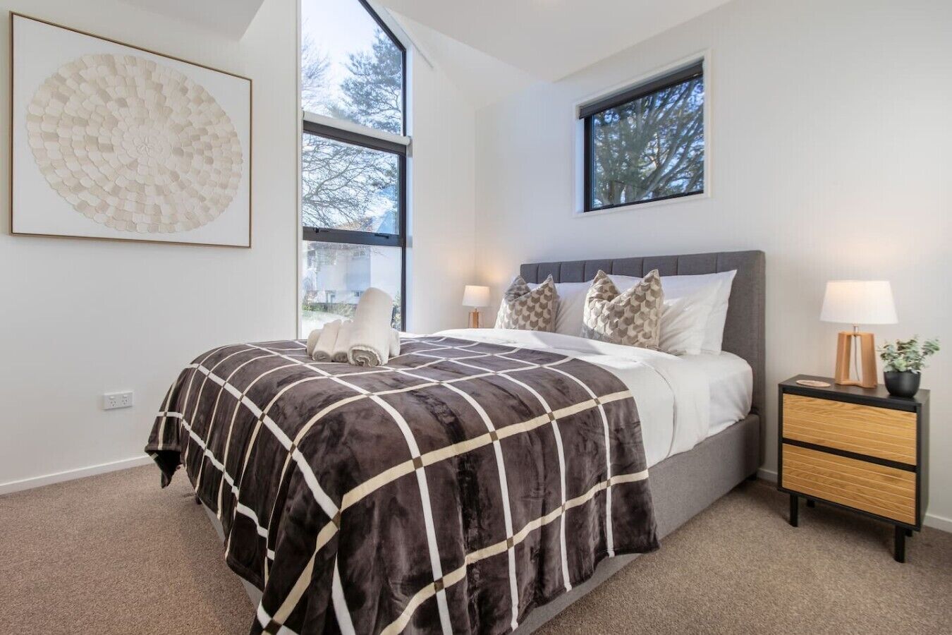 A bedroom with a bed, bedside tables, a window, and a wall-mounted artwork.