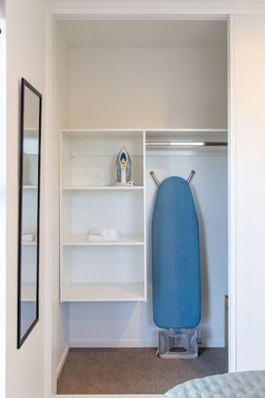 A walk-in closet with shelves, a hanging rack, and a small ironing board. - Peaceful Merivale Hideaway - Parkside + Parking (Christchurch)