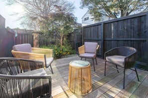 An outdoor patio area with wicker furniture, a round table, and a wooden fence. - Peaceful Merivale Hideaway - Parkside + Parking (Christchurch)