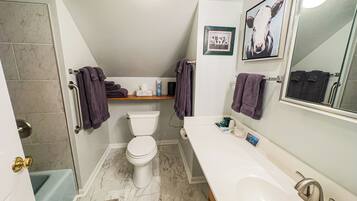 A bathroom with a toilet, sink, and shower. There are towels and toiletries on the counter.