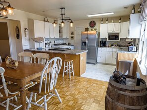 A kitchen with white cabinets, a stainless steel refrigerator, a wooden dining table with chairs, and a bar area with stools.