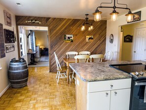 A kitchen with a wooden herringbone floor, a herringbone wall, a wooden dining table with white chairs, a kitchen island with a granite countertop, and a hanging light fixture.