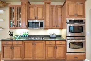 A kitchen with wooden cabinets, a microwave, a toaster, and a stove. - Spacious Luxury Home | Beach Access | Resort Living- Sleeps 10 (New Smyrna Beach)