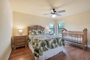 A bedroom with a bed, nightstand, dresser, crib, and a ceiling fan. - Spacious Luxury Home | Beach Access | Resort Living- Sleeps 10 (New Smyrna Beach)