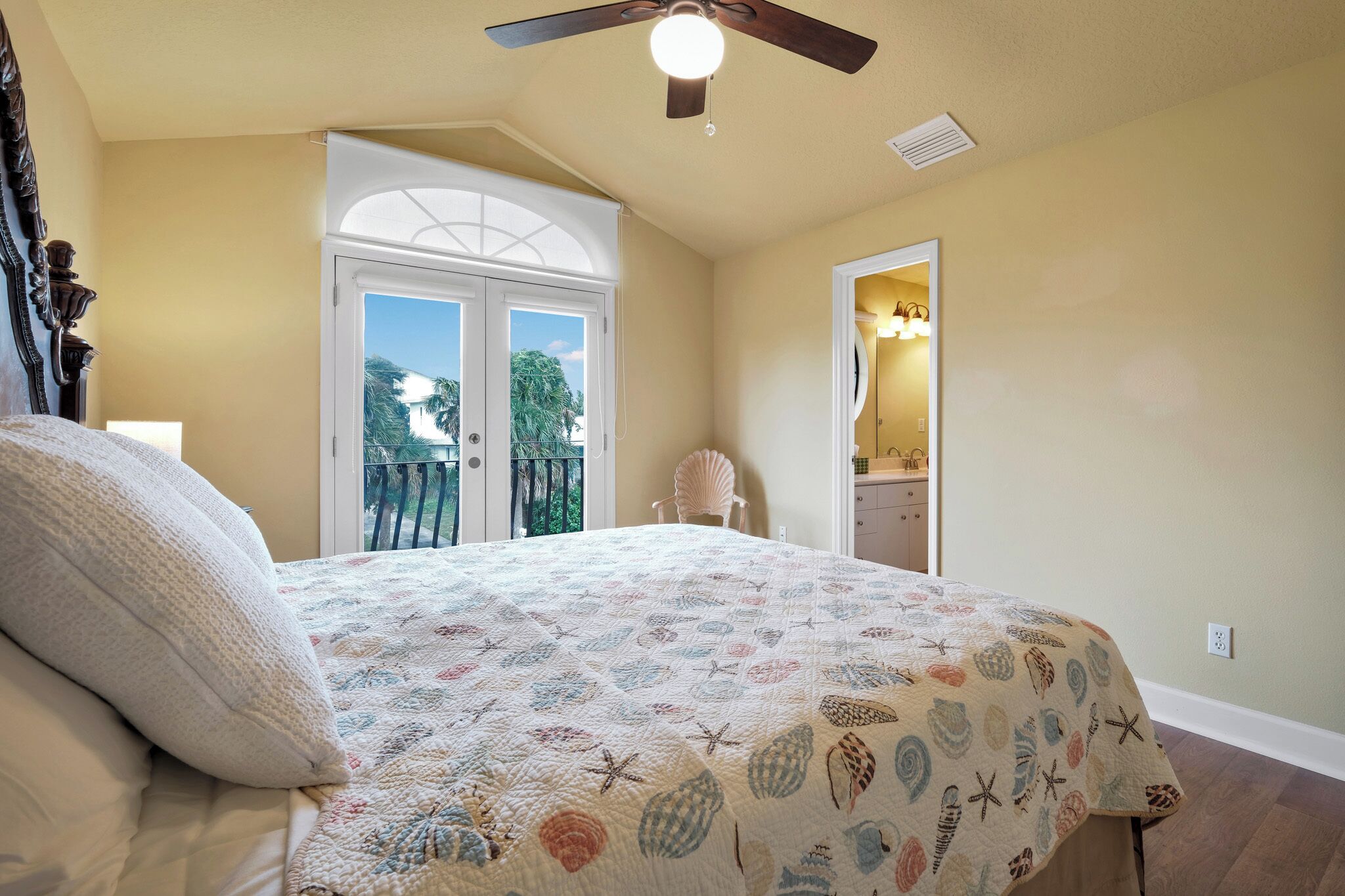 Une chambre à coucher avec un lit, un ventilateur de plafond, une fenêtre et une porte donnant sur un balcon.
