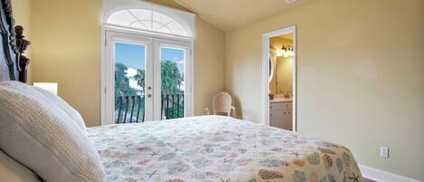 Une chambre à coucher avec un lit, un ventilateur de plafond, une fenêtre et une porte donnant sur un balcon.