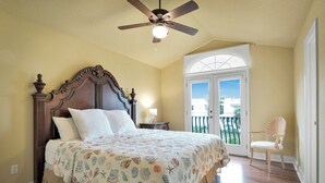 Una camera da letto con un letto grande, un ventilatore a soffitto, un comodino, una sedia e vista sull'esterno attraverso una porta.