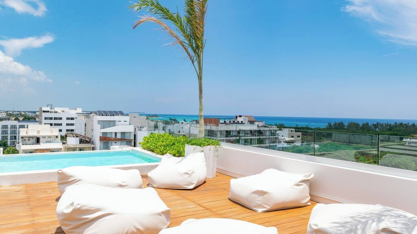 Une terrasse sur le toit avec une piscine, des coussins blancs et une vue sur la mer et les bâtiments.