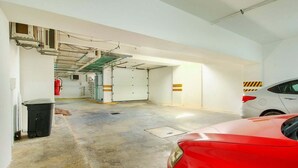 Un parking avec une voiture rouge, un extincteur et une poubelle.