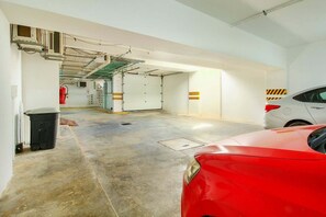 Eine Parkgarage mit einem roten Auto, einem Feuerlöscher und einem Müllbehälter.