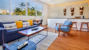 Un salon moderne avec un canapé, une table basse et un fauteuil bleu. On y trouve également un coin cuisine avec un évier et des objets décoratifs accrochés au mur.